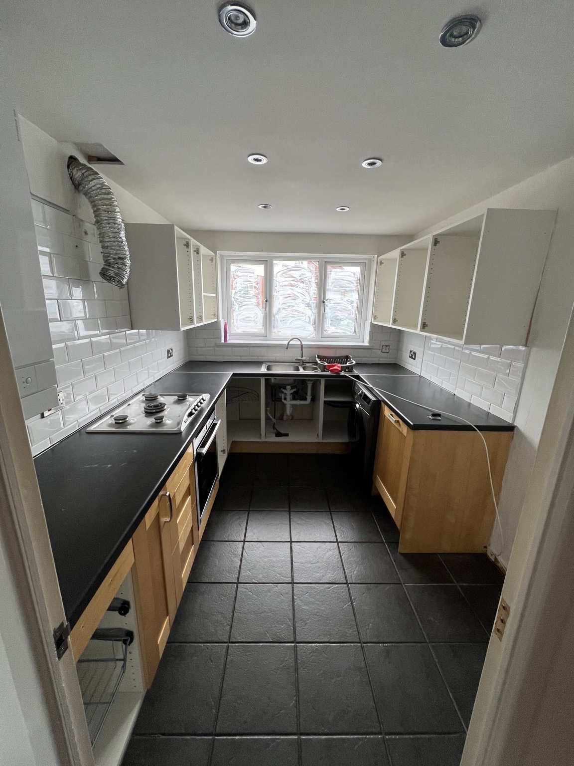Kitchen before the refit, with timber-effect doors, dark worktops and black floor tiles