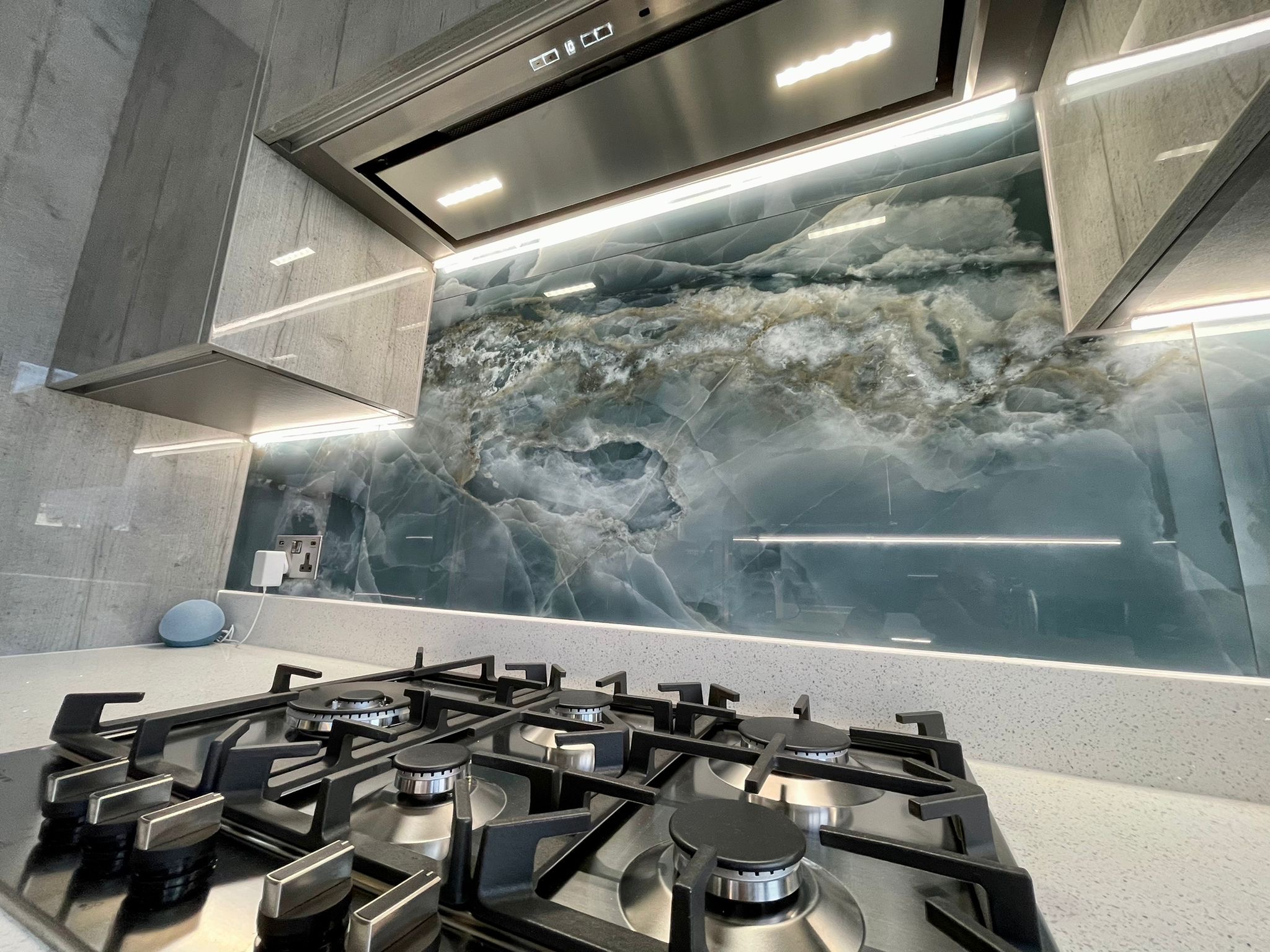 SMC kitchen installation with a gas hob, blue stone-effect splashback and illuminated fitted cabinets