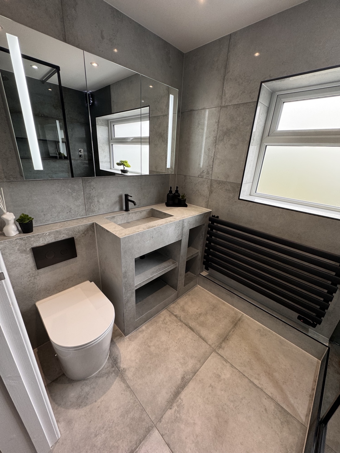 Completed grey tiled bathroom with a custom tiled basin, wall-hung toilet and black radiator