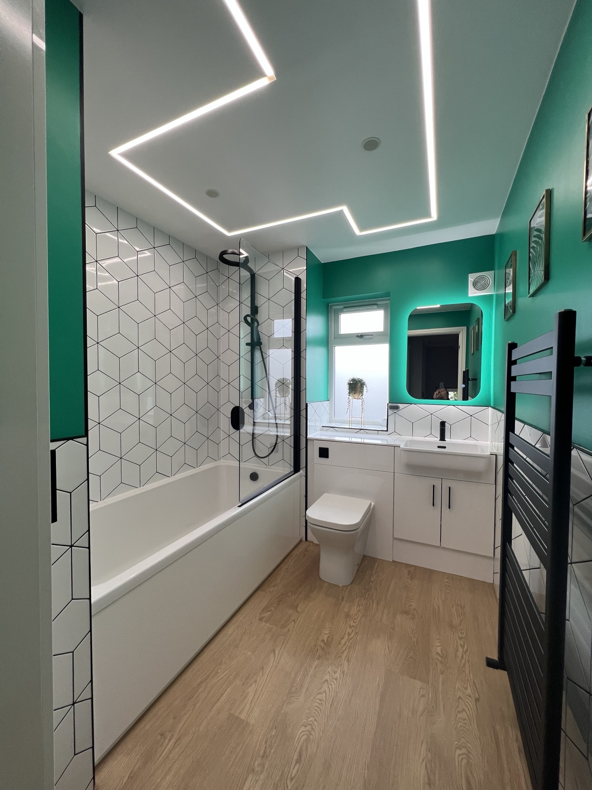 Same bathroom after refurbishment with geometric tiles, black fittings and teal walls
