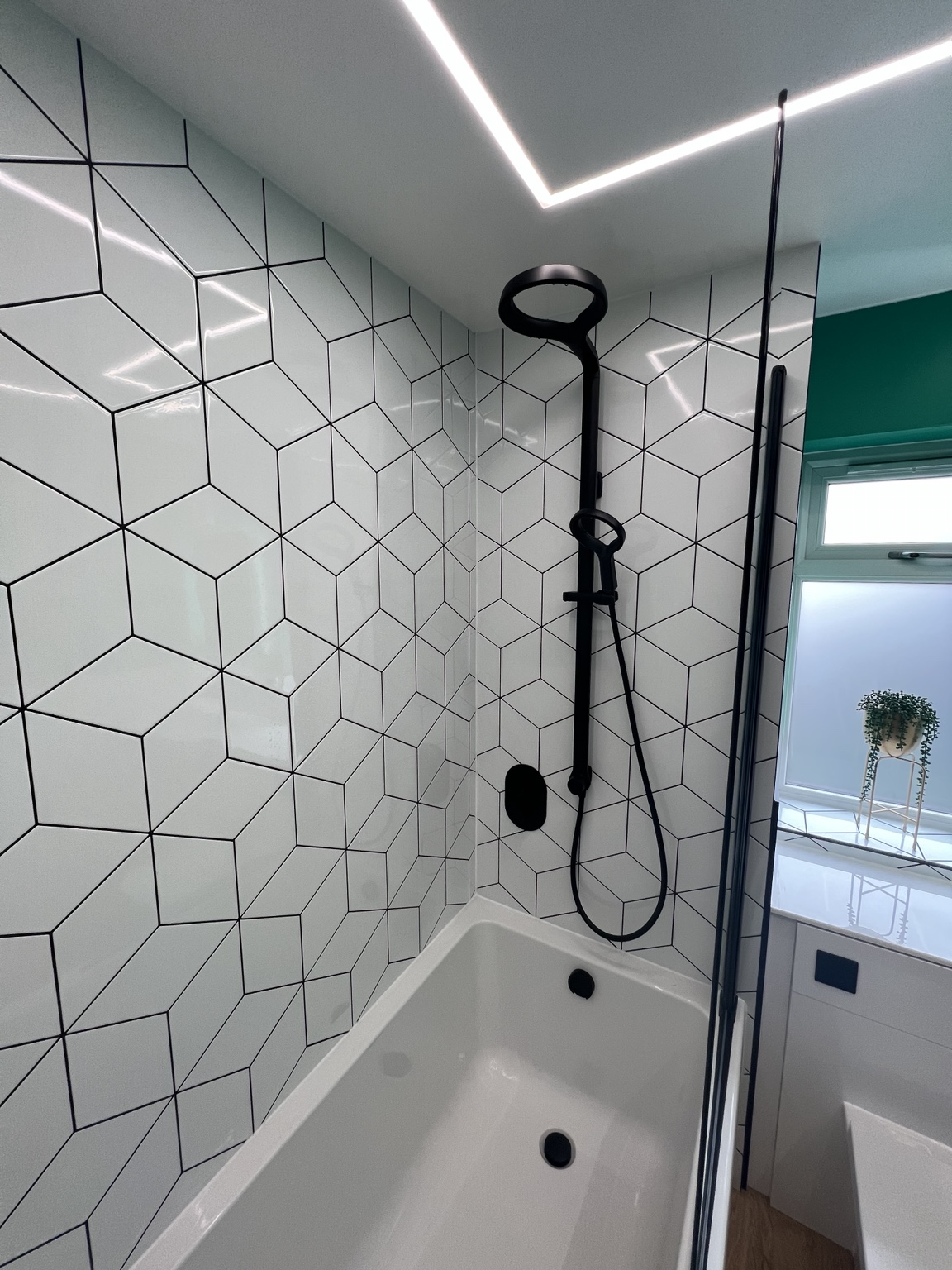 Geometric wall tiles and black shower fittings above the bath
